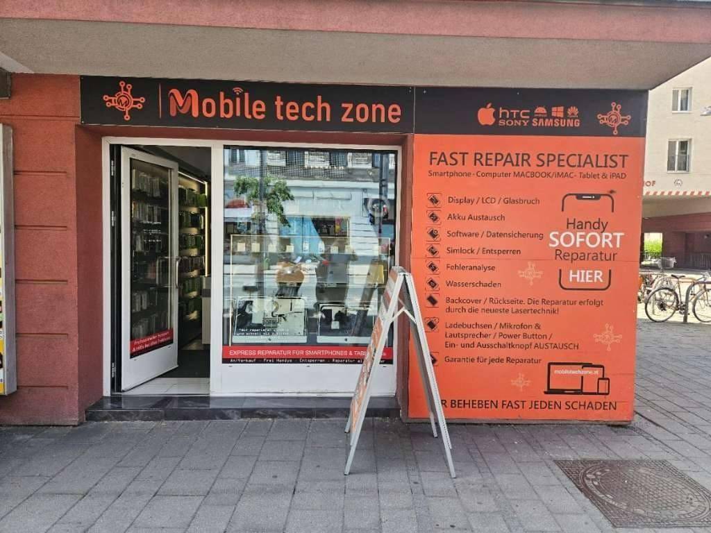 Eingangsbereich des Geschäfts 'Mobile tech zone' mit auffälliger orangefarbener Beschilderung und Werbetafel.