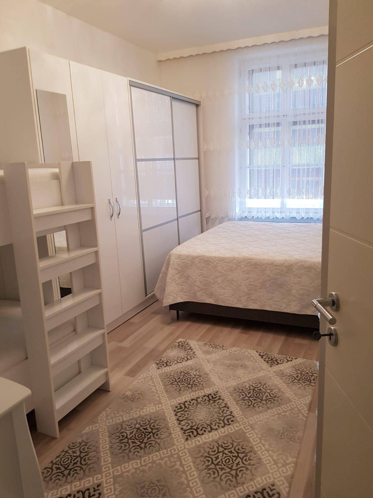 Kinderzimmer mit Etagenbett, Doppelbett und weißem Schiebetürenschrank, hell und funktional eingerichtet.