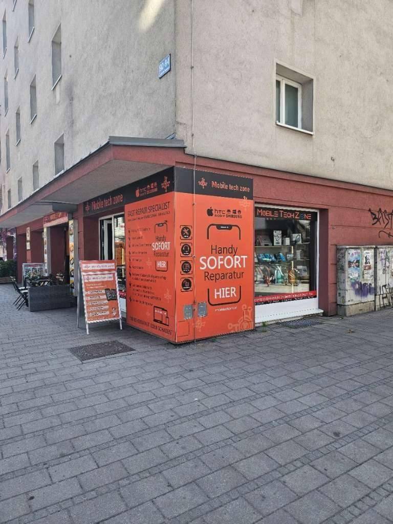Außenansicht des Geschäfts 'Mobile tech zone' an einer Straßenecke mit umliegenden Gebäuden und Bürgersteig.