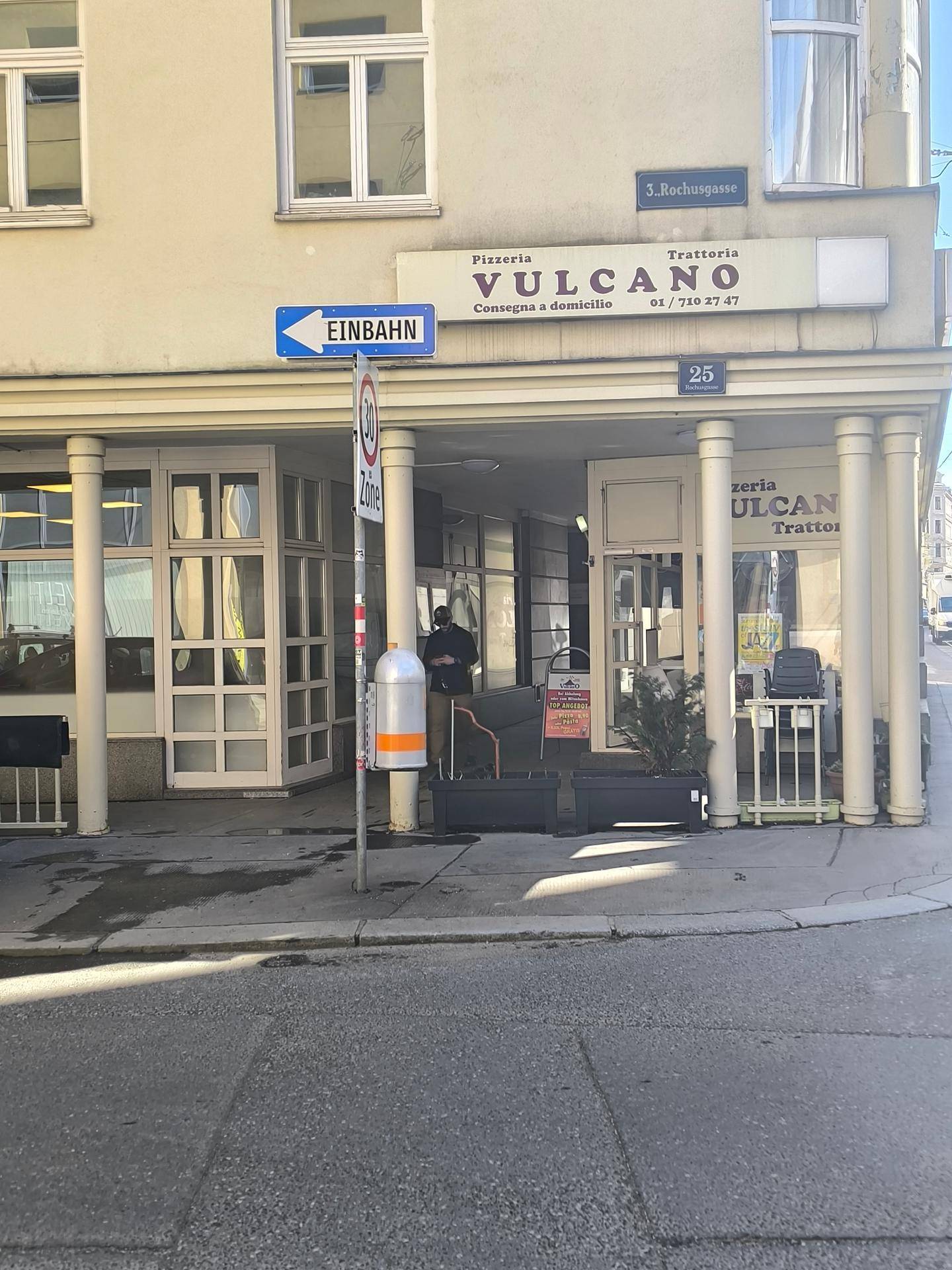 Eingangsbereich eines Gebäudes mit Pizzeria und Straßenschildern in einer städtischen Umgebung.