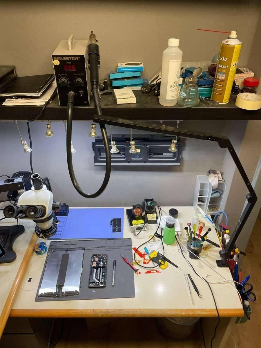 Spezialisierter Reparaturtisch mit Mikroskop, Lötstation und verschiedenen Werkzeugen für Elektronikreparaturen.