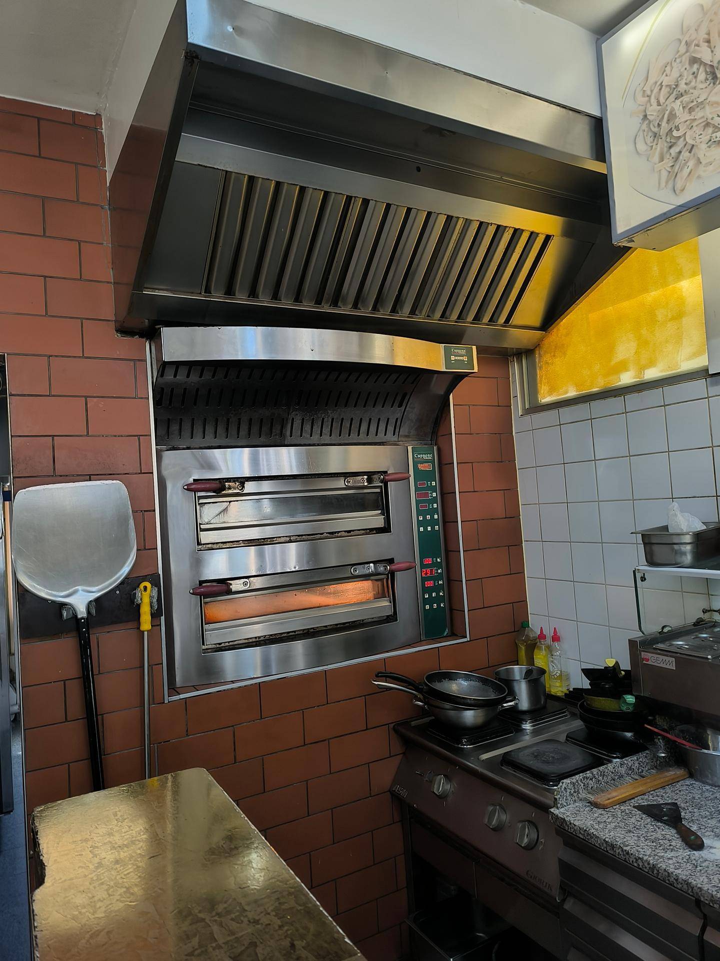 Professionelle Küche mit großem Pizzaofen, Dunstabzugshaube und Gasherd.