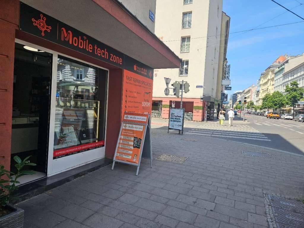 Blick auf eine belebte Stadtstraße mit einem Technikgeschäft und weiteren Gebäuden im Hintergrund.