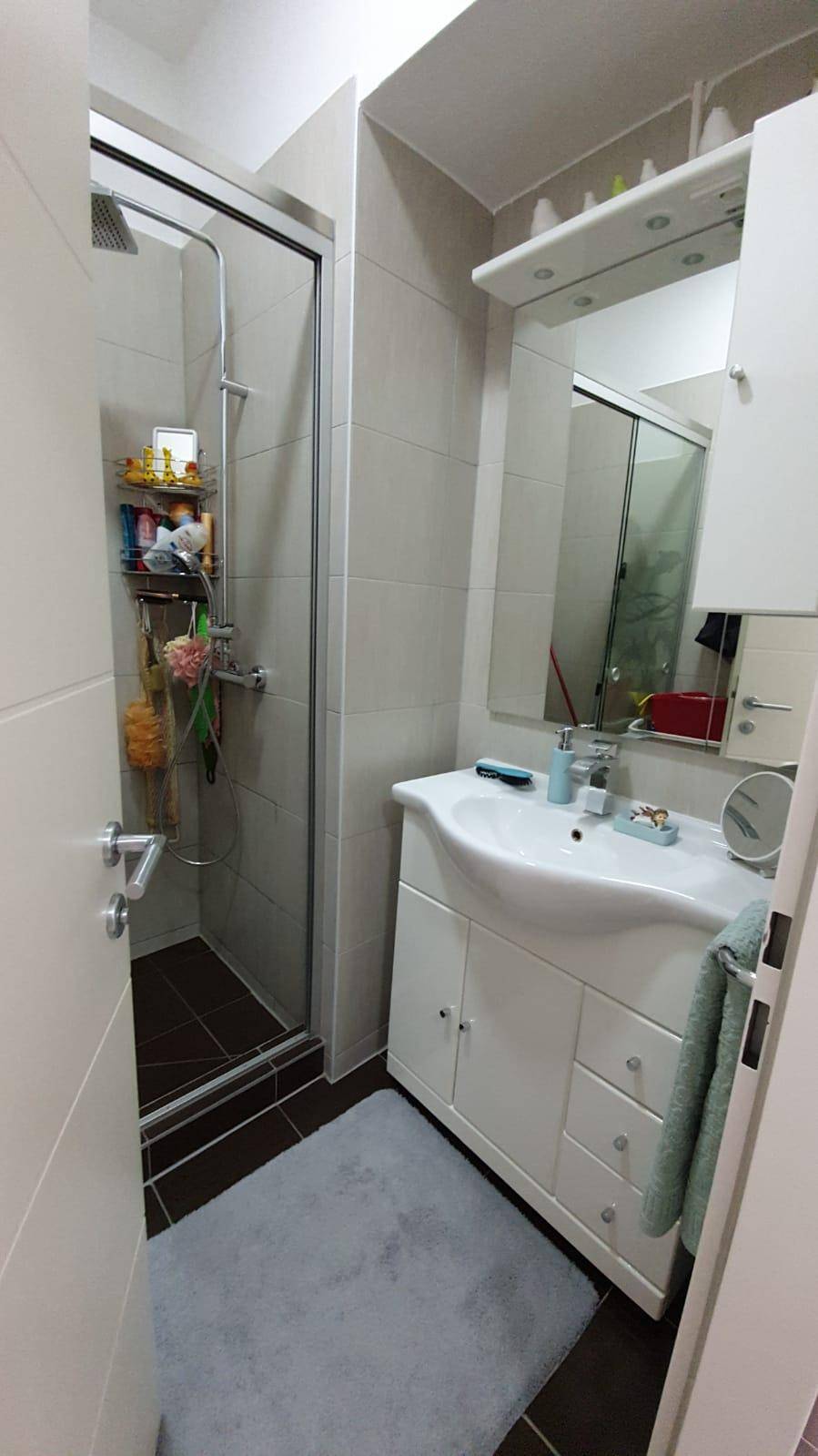 Modernes Badezimmer mit Duschkabine, Waschbecken mit Unterschrank und hellen Fliesen.