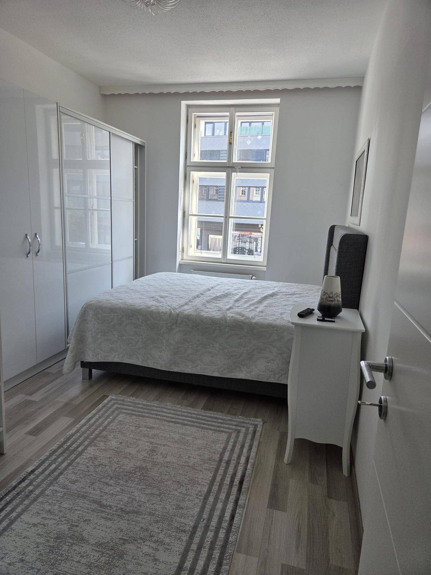 Helles Schlafzimmer mit Doppelbett, weißem Kleiderschrank und einem Fenster mit Blick nach draußen.