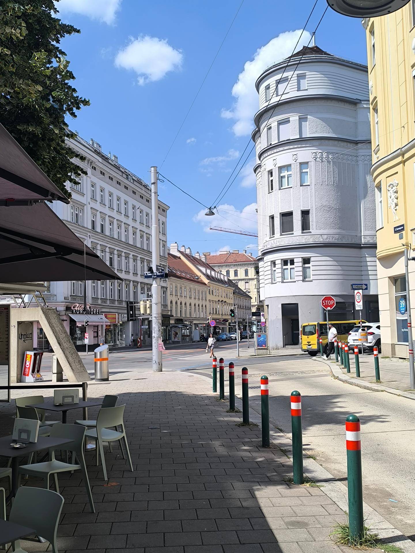 Straßenecke mit einem Café im Vordergrund, historischen Gebäuden und einer ruhigen Stadtstraße.