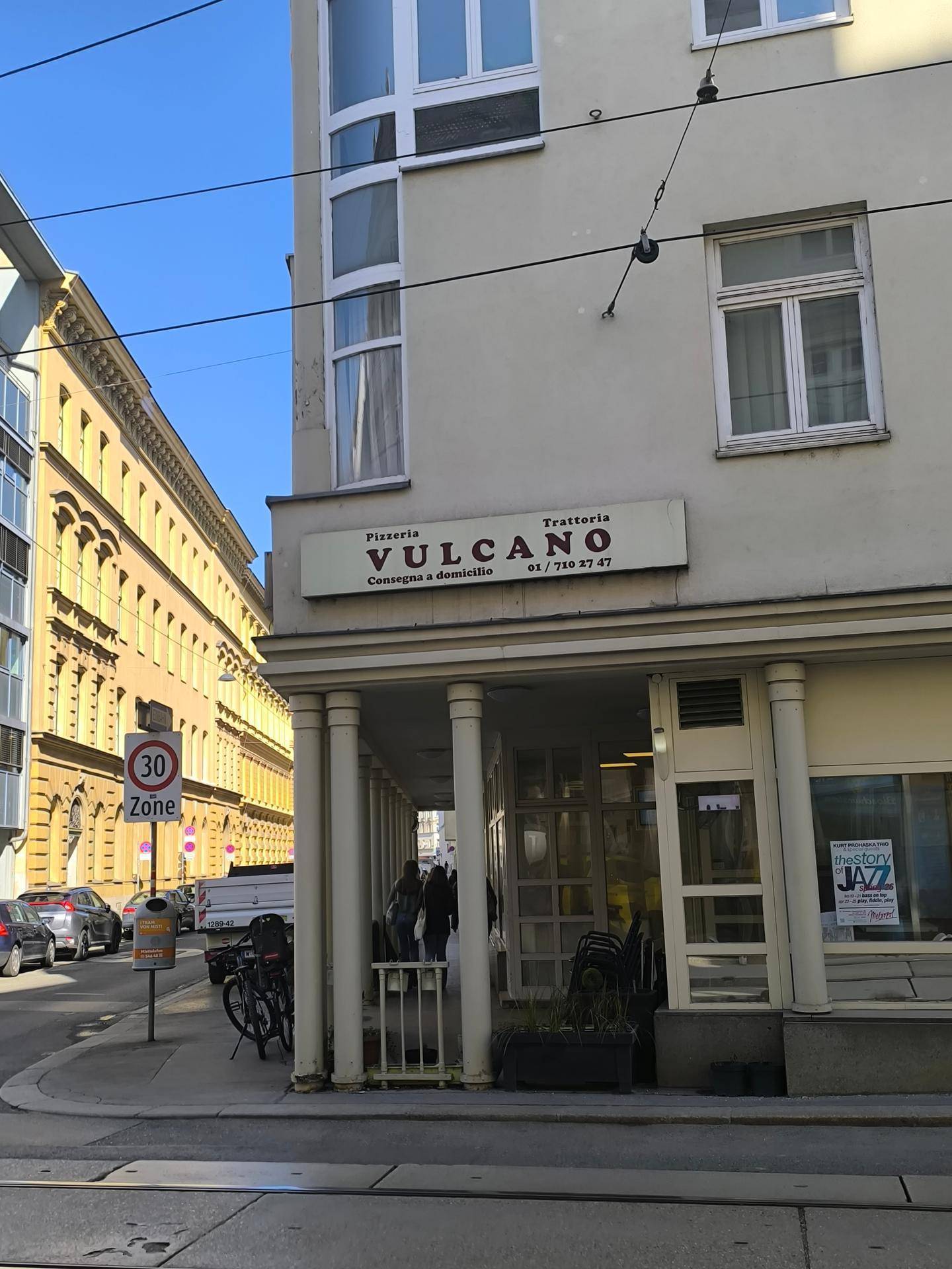 Fassade eines Eckgebäudes mit Pizzeria-Schild und Blick auf die belebte Straße.
