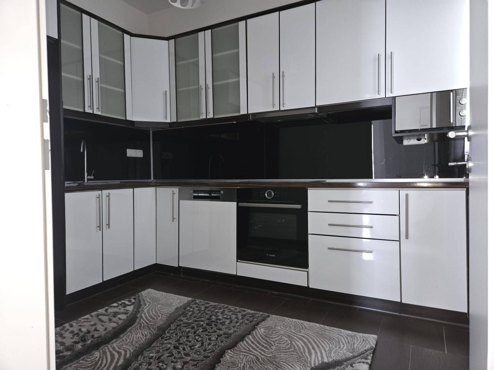Moderne Küche mit weißen Hochglanzfronten, dunkler Arbeitsplatte und integrierten Geräten.
