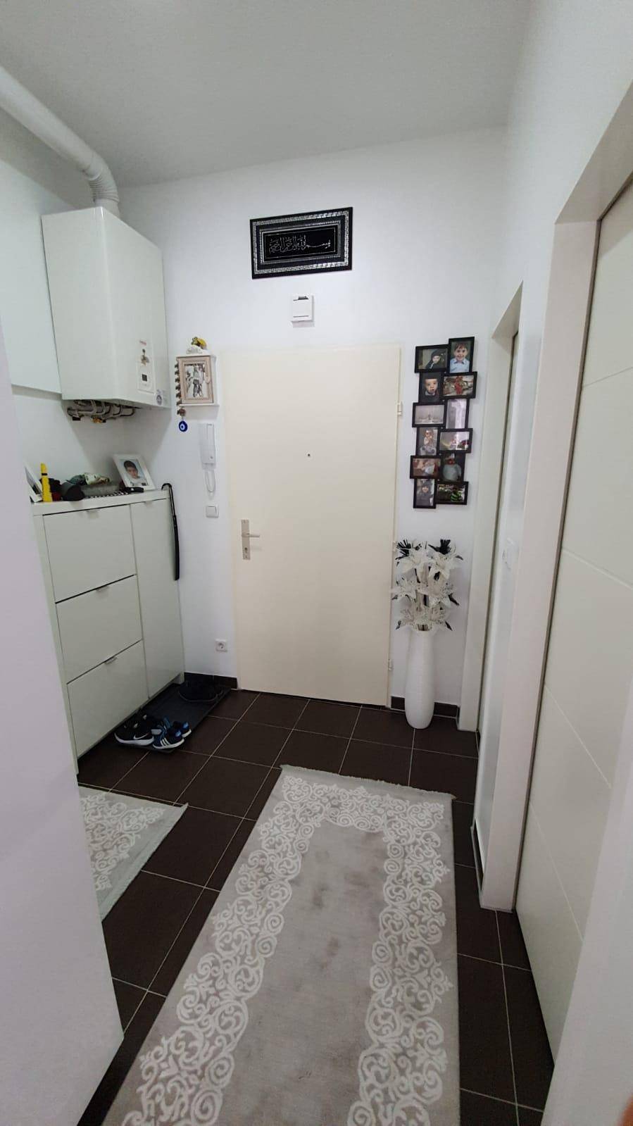 Heller Eingangsbereich mit Fliesenboden, Schuhschrank und einer Gastherme an der Wand.