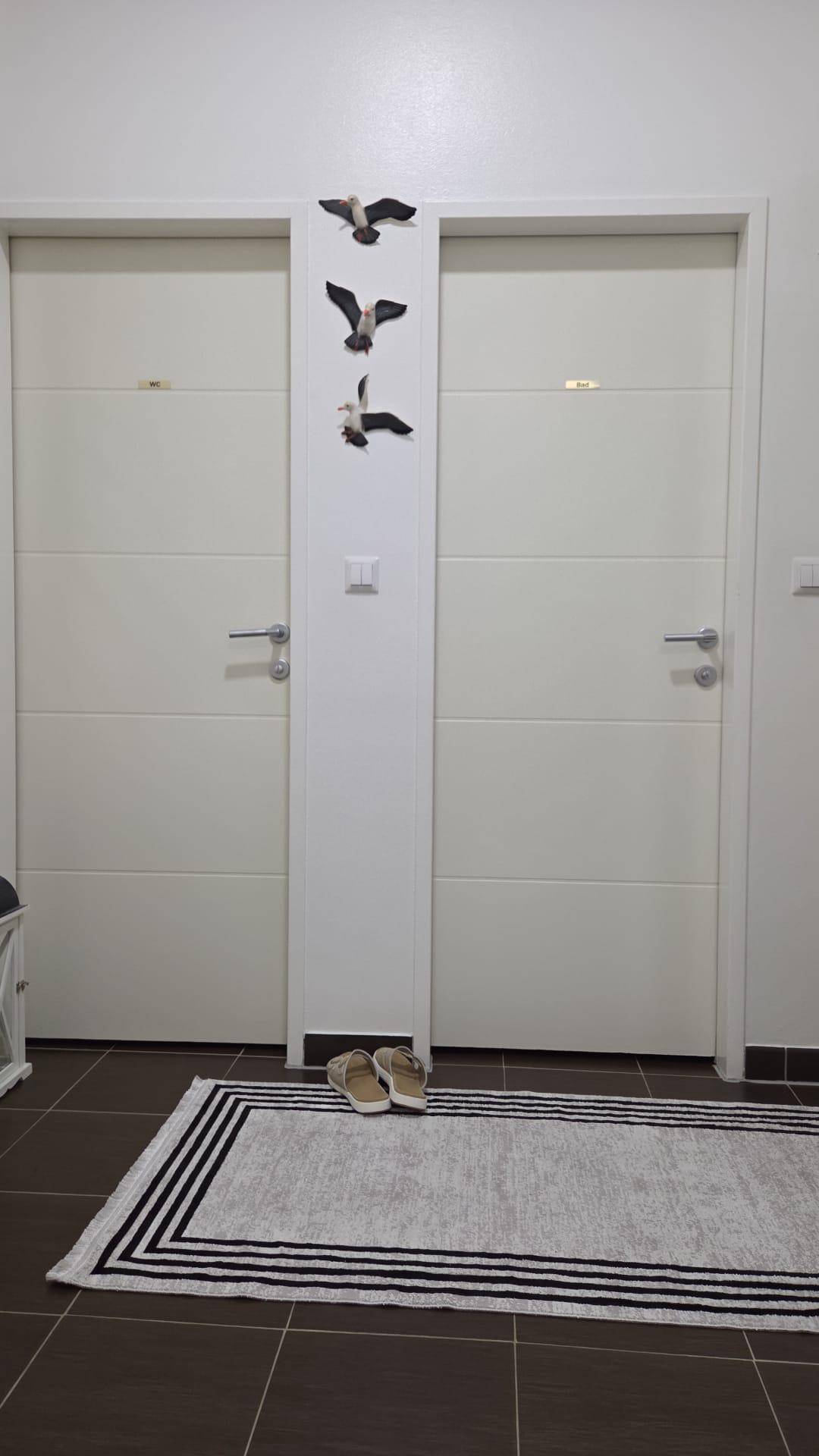 Heller Flur mit zwei weißen Türen, einem Teppich und dunklen Fliesen auf dem Boden.