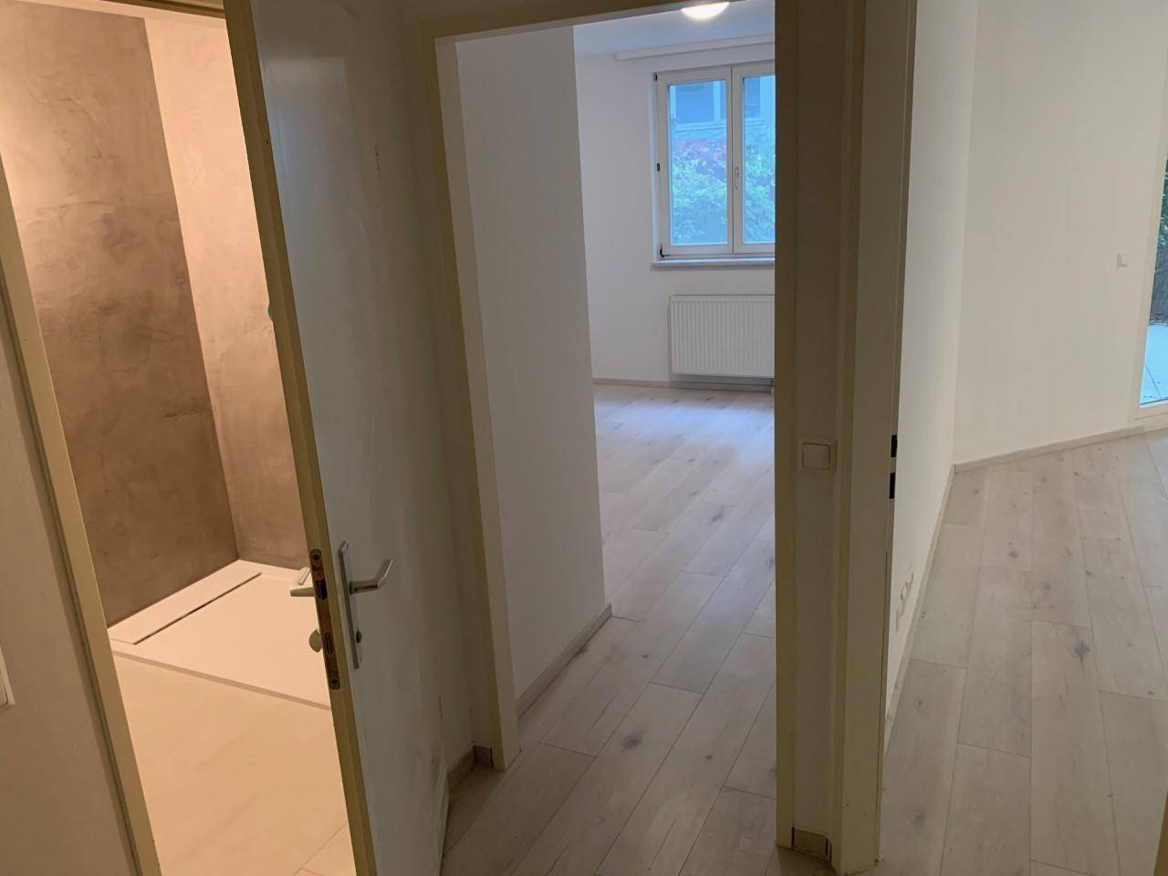 Heller Flur mit modernem Laminatboden, der zu weiteren Zimmern und einem Fenster führt.