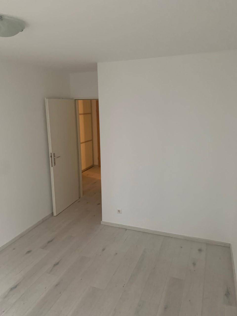Leerer Raum mit hellem Laminatboden und weiß gestrichenen Wänden, bereit zur individuellen Gestaltung.
