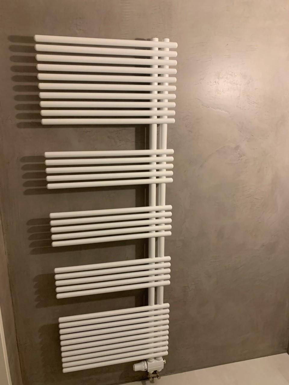 Moderner weißer Handtuchheizkörper an einer grauen Wand im Badezimmer.