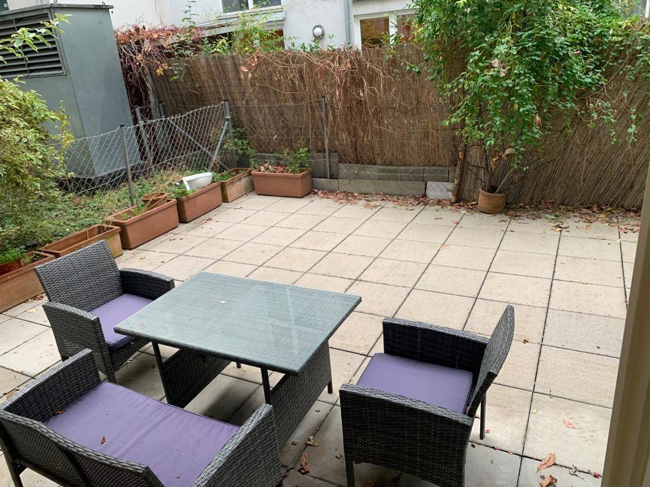 Pflasterter Terrassenbereich mit Sitzgelegenheiten und einer natürlichen Begrenzung durch eine Hecke.