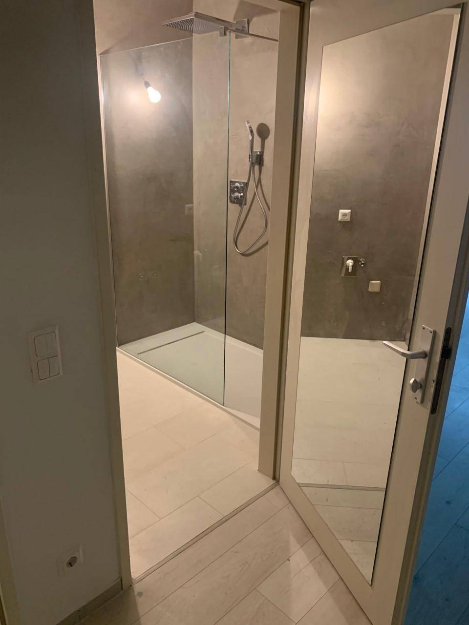 Elegante begehbare Dusche mit Glasabtrennung und moderner Regendusche in hellem Ambiente.