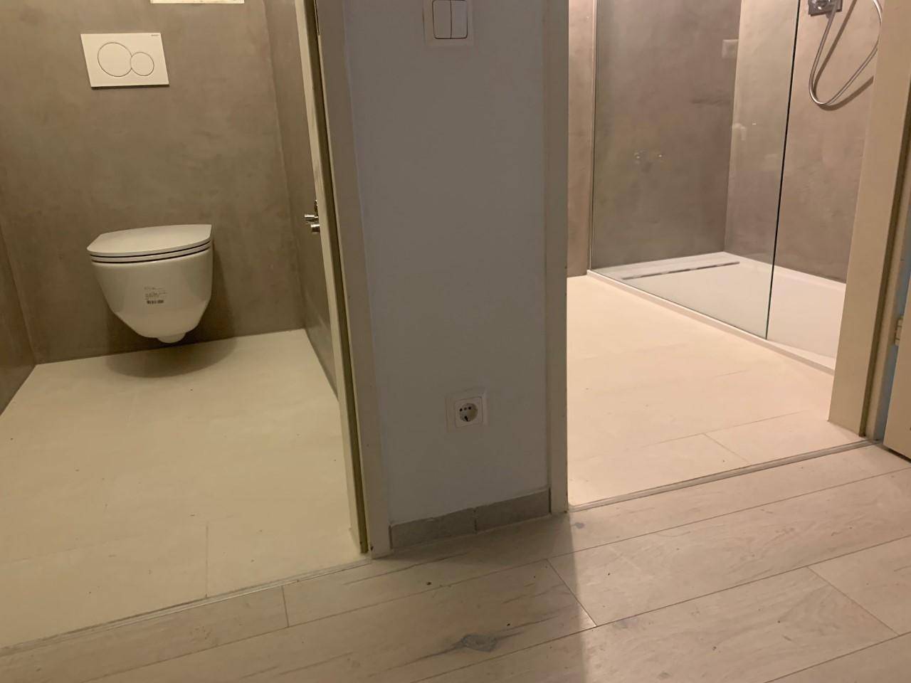 Modernes Badezimmer mit wandhängendem WC und einer geräumigen, ebenerdigen Dusche.
