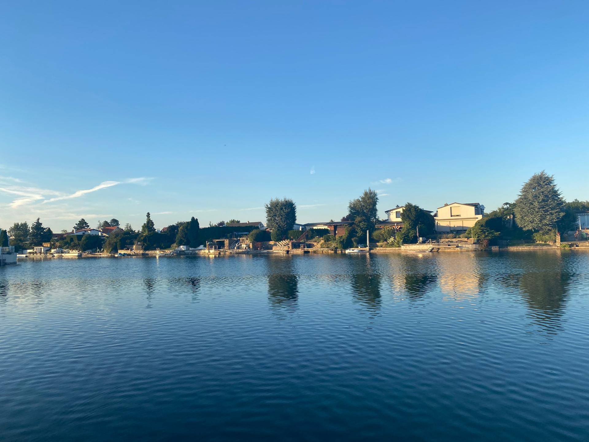 Ruhige Seeansicht mit Häusern am Ufer unter einem weiten, klaren blauen Himmel.