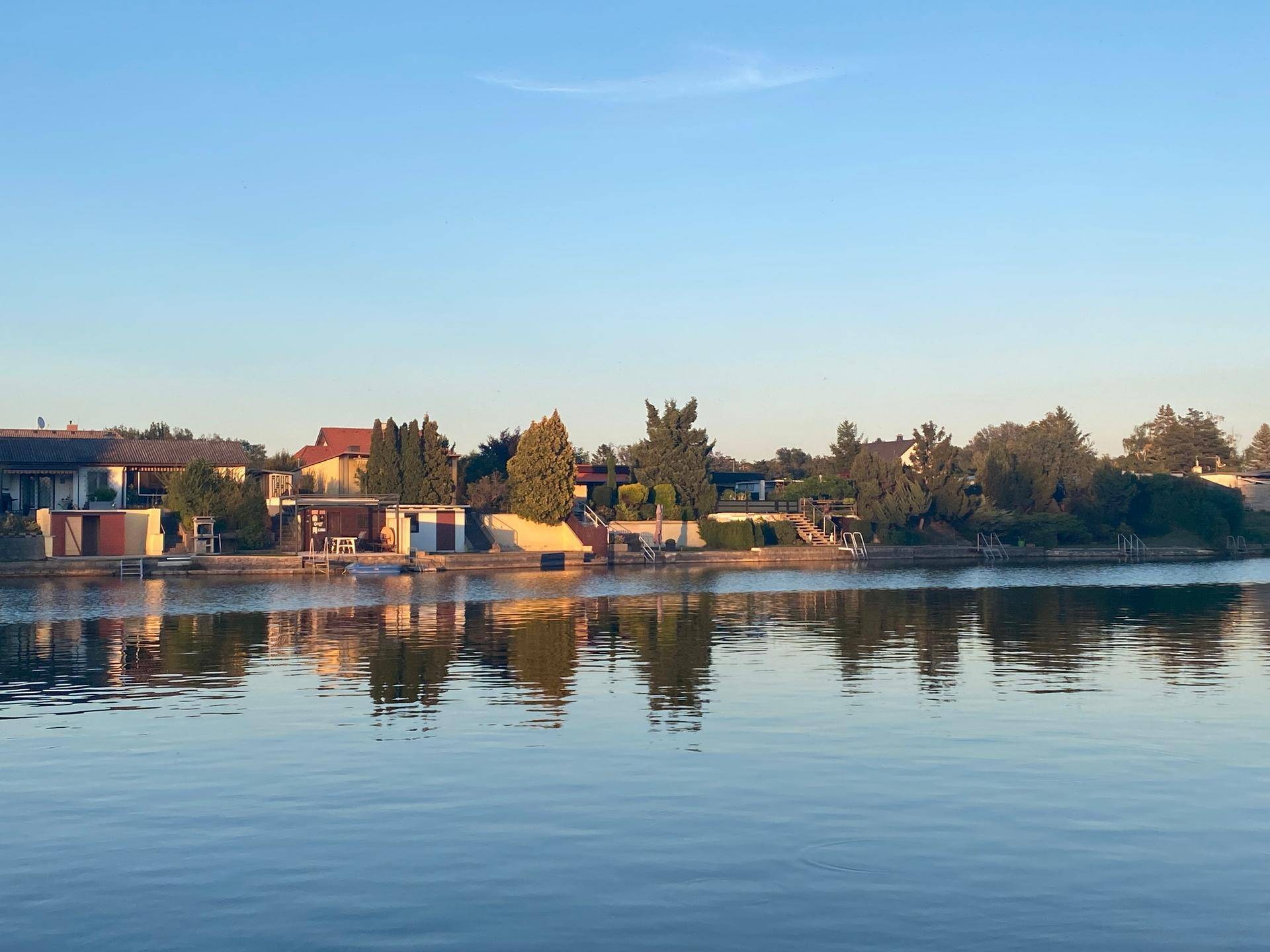 Malerische Abendstimmung am See mit spiegelnden Häusern und Bäumen am Ufer.