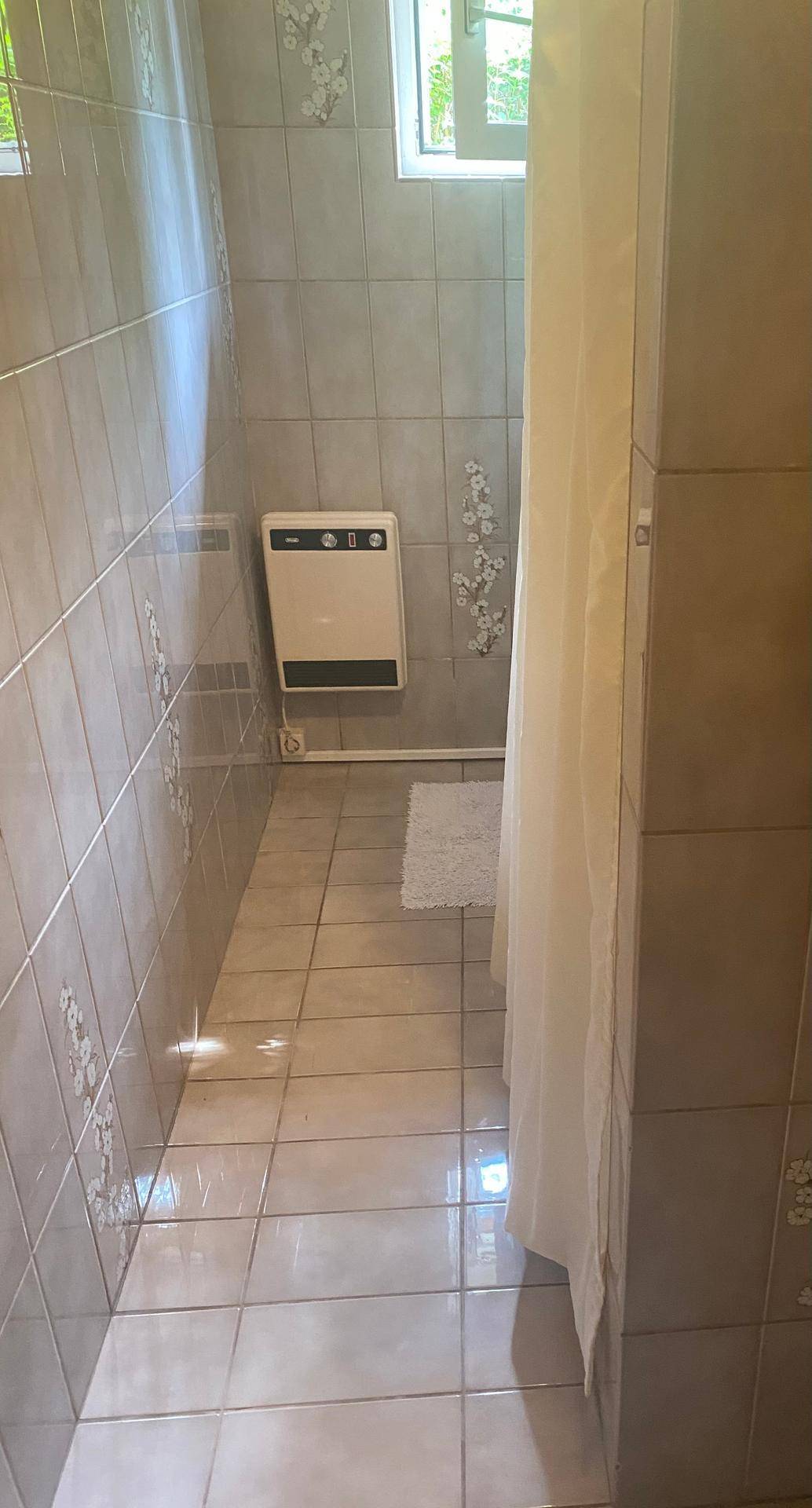 Kleines Badezimmer mit hellen Fliesen, Duschbereich und einem Fenster für Tageslicht.