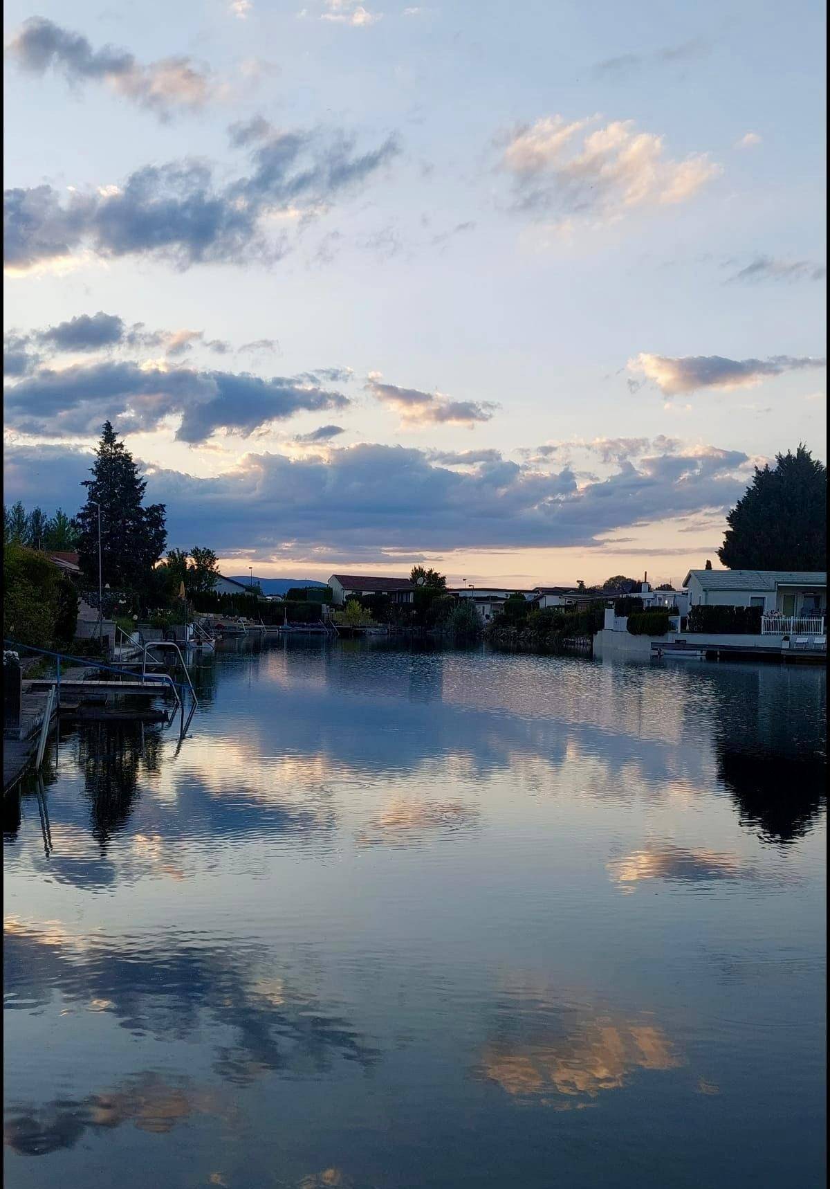 Malerischer Sonnenuntergang über dem See mit ruhigem Wasser und Häusern am Horizont.