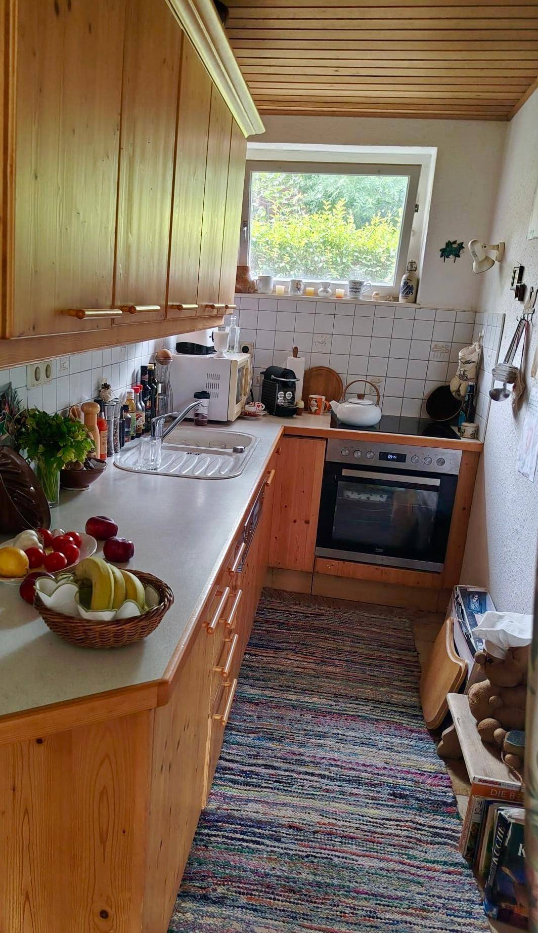 Funktionale Küche mit Holzschränken, Arbeitsplatte und Fenster für natürliches Licht.