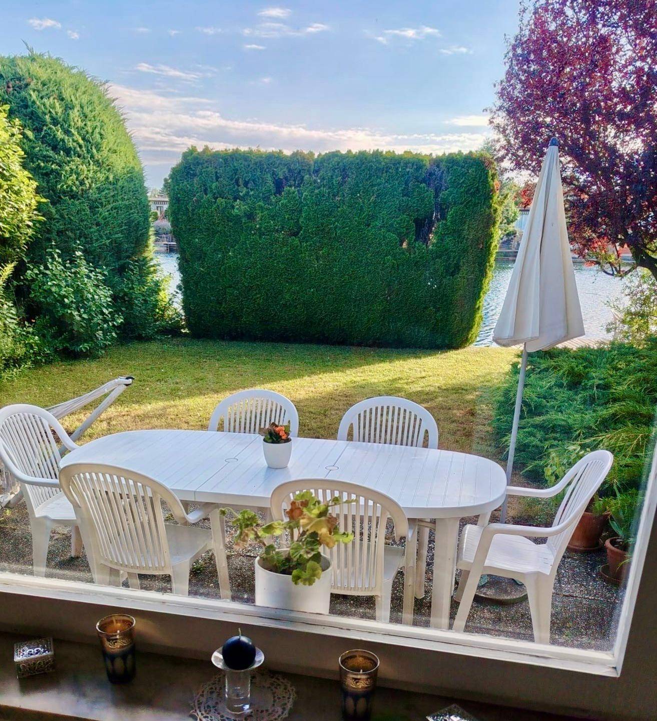 Blick aus dem Fenster auf den gepflegten Garten mit Sitzgelegenheiten und hoher Hecke.