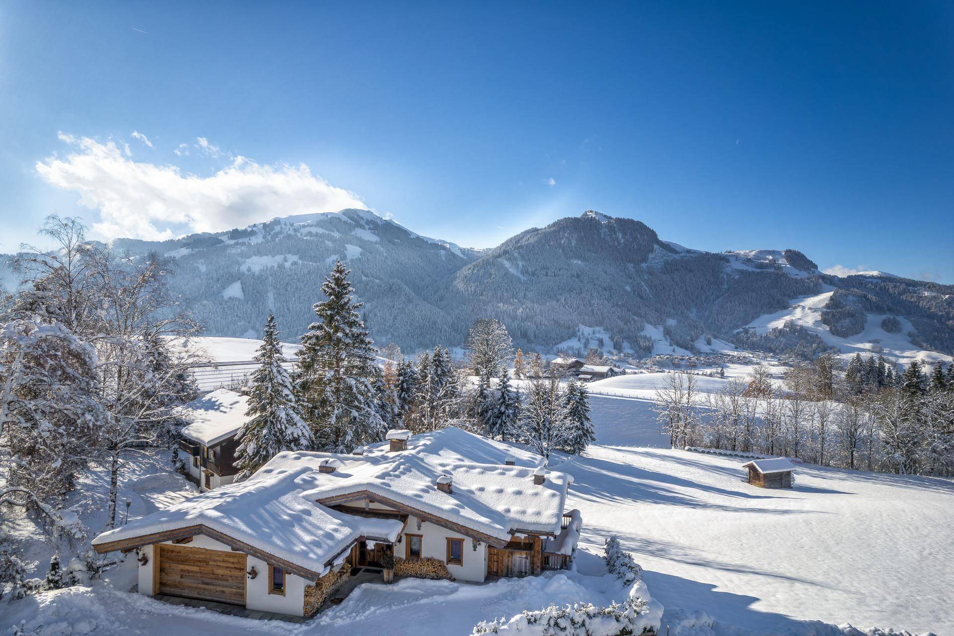 Idyllisches Chalet in winterlicher Berglandschaft mit schneebedeckten Dächern und Bäumen.