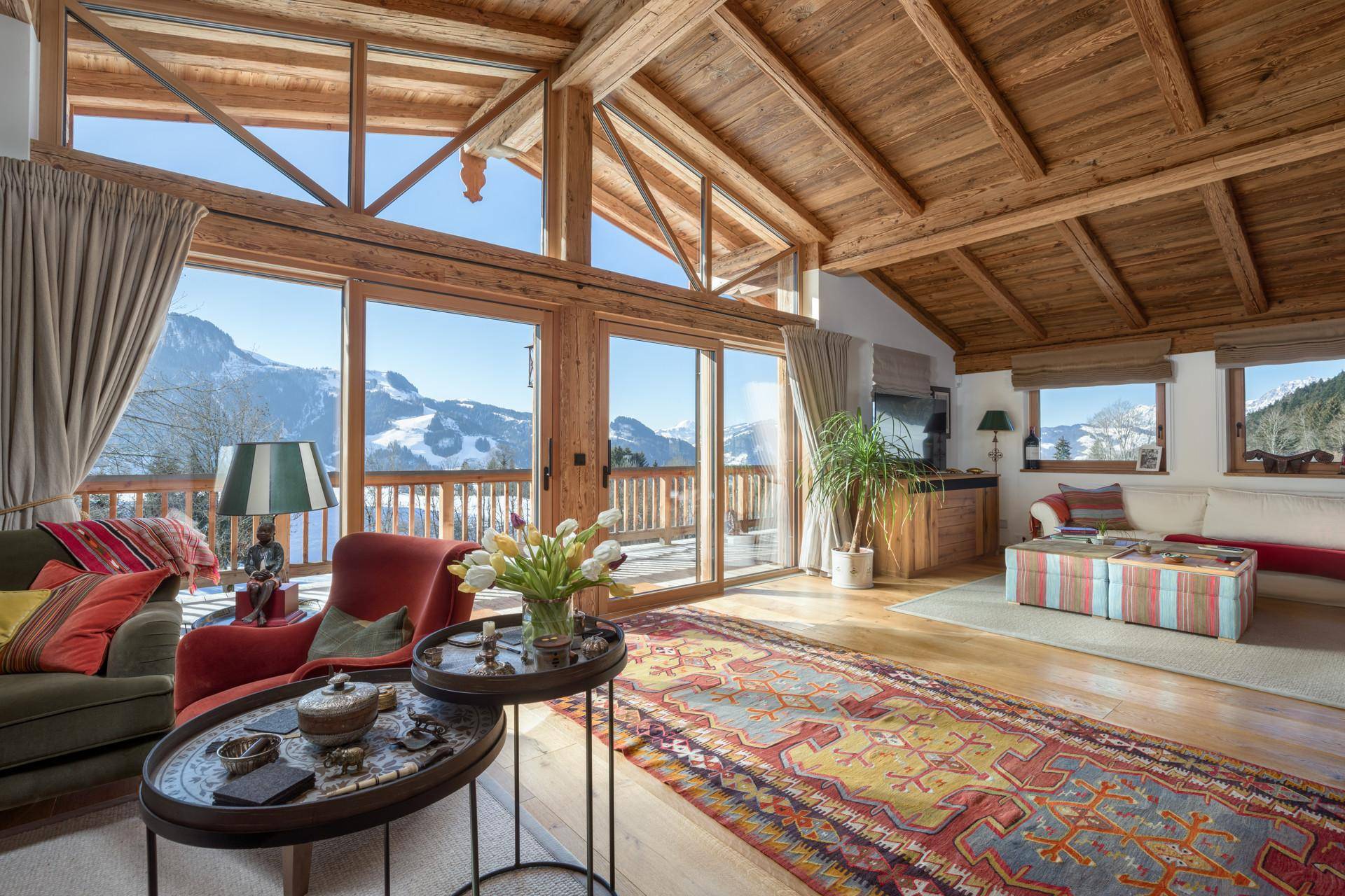 Lichtdurchflutetes Wohnzimmer mit hohen Holzdecken, großen Fenstern und Bergblick.