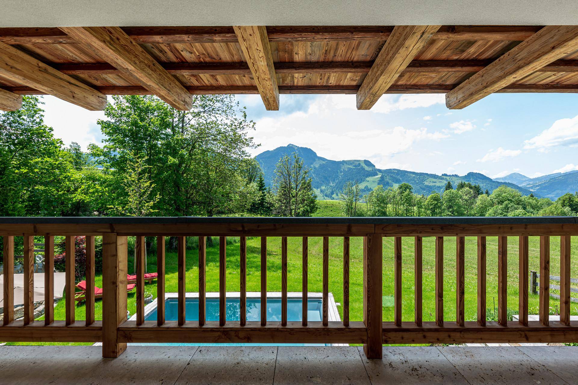 Blick vom Holzbalkon auf den Poolbereich und die umliegende grüne Berglandschaft.