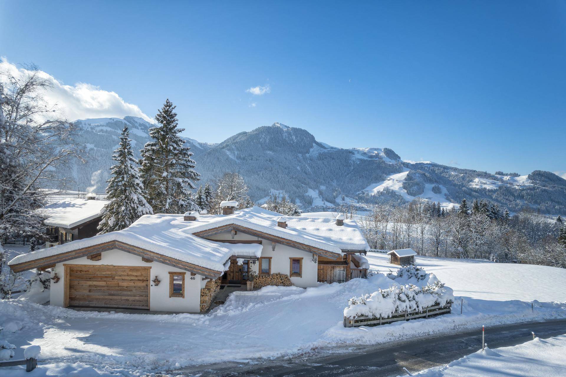 Alpenchalet in sonniger Winterlandschaft mit schneebedeckten Dächern und Holzfassade.