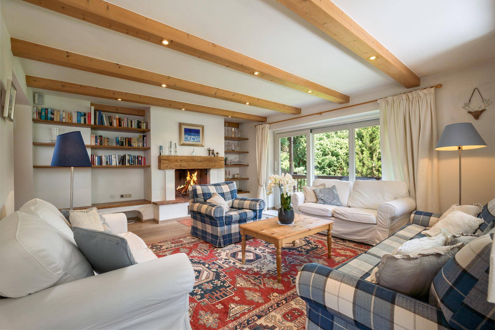 Helles Wohnzimmer mit Kamin, Bücherregalen und Zugang zur Terrasse mit Grünblick.