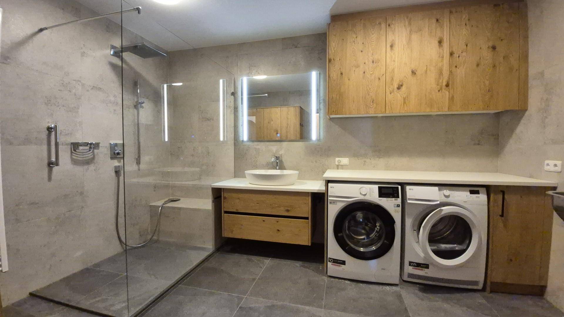 Modernes Badezimmer mit ebenerdiger Dusche, Einzelwaschbecken, Fliesenboden und Haltegriffen.