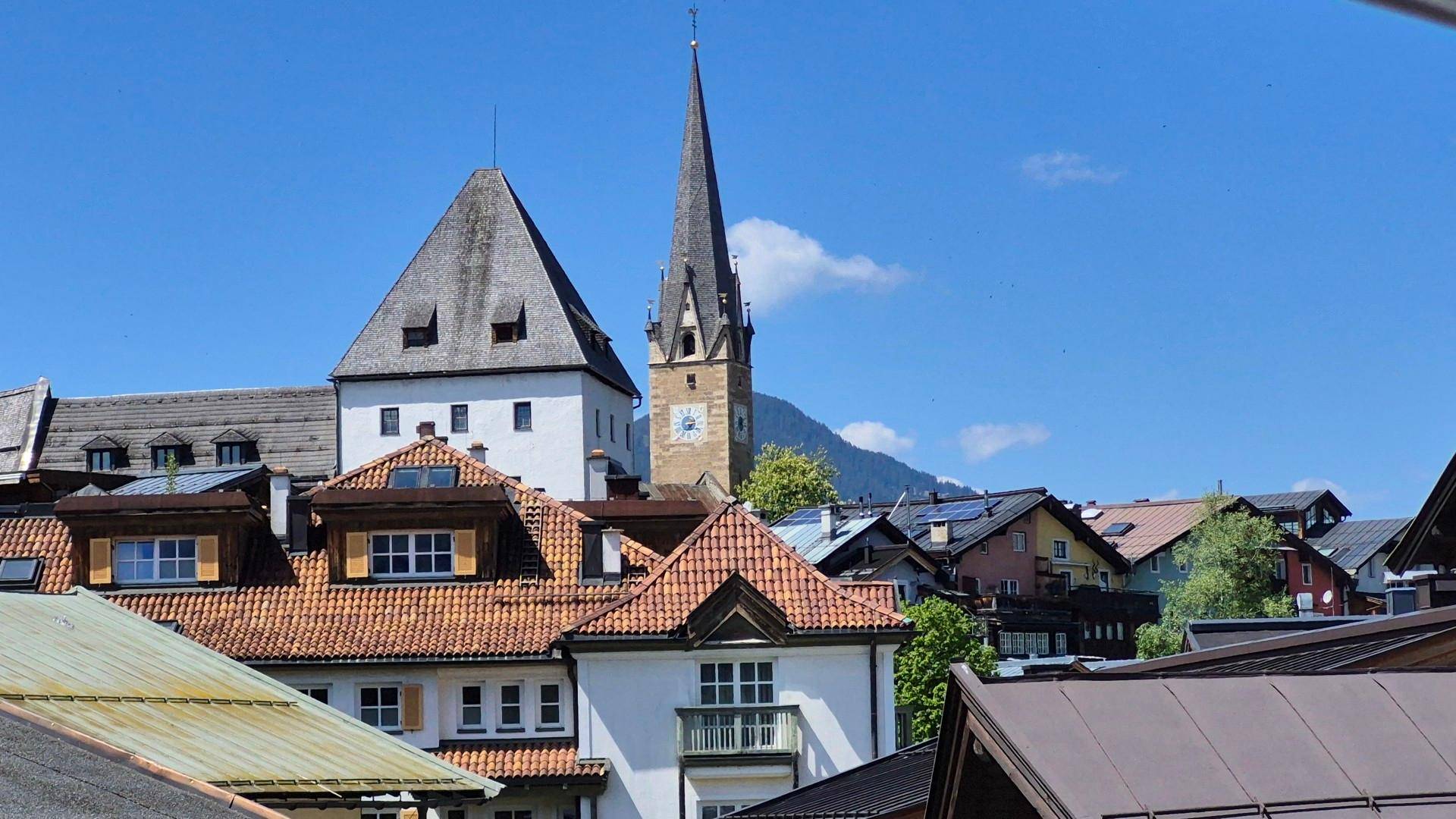 Panoramablick über eine charmante Alpenstadt mit traditionellen Gebäuden, Kirchturm und Bergen im Hintergrund.