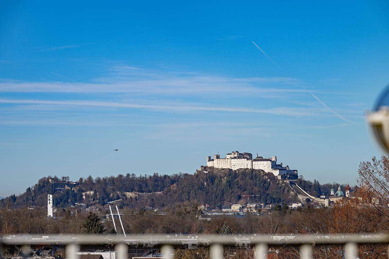 Panoramablick auf die Festung Hohensalzburg und die umliegende Stadtlandschaft unter blauem Himmel.