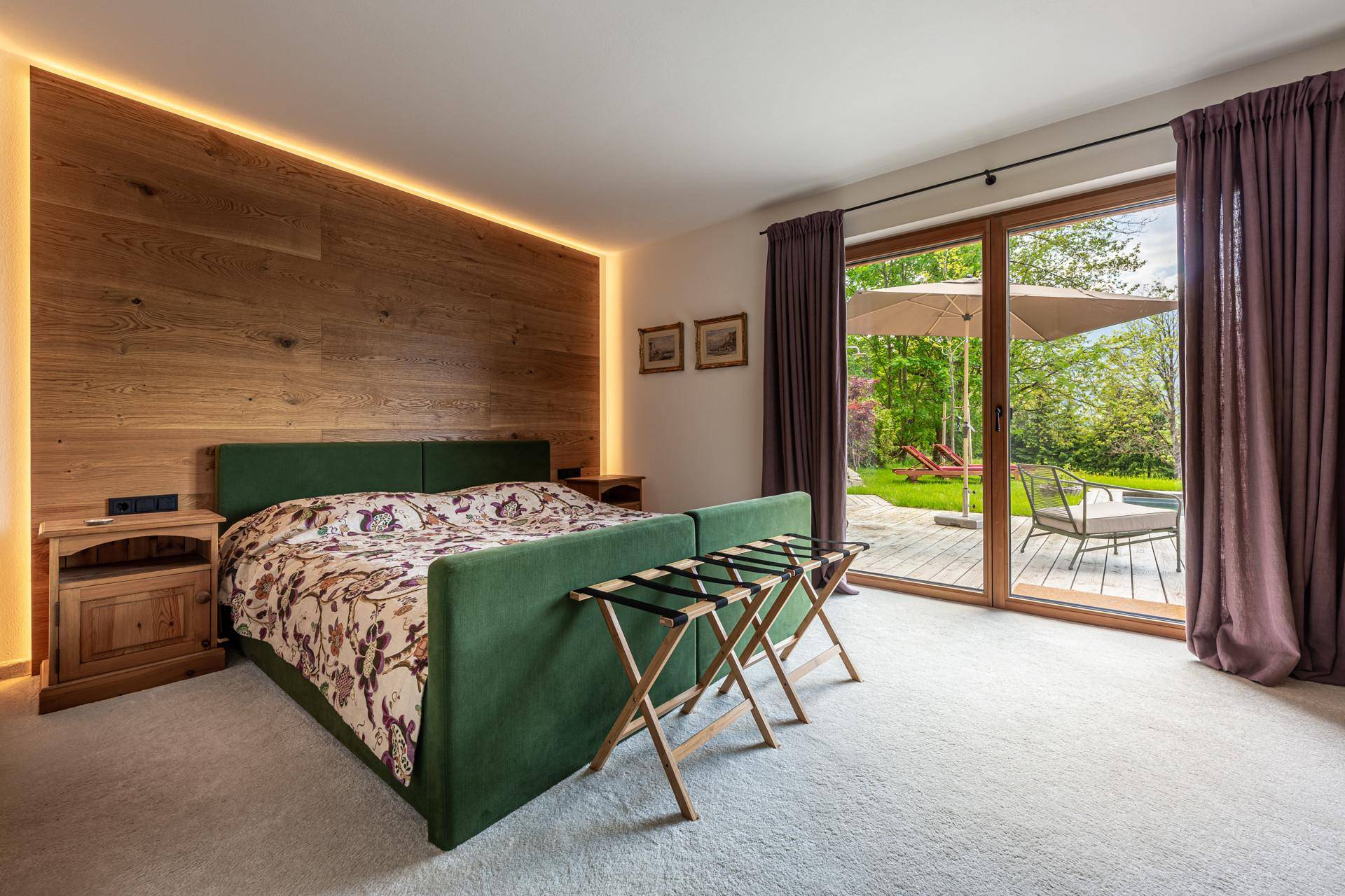 Helles Schlafzimmer mit grünem Bett, Holzwand und direktem Zugang zu einer Terrasse oder Gartenbereich.