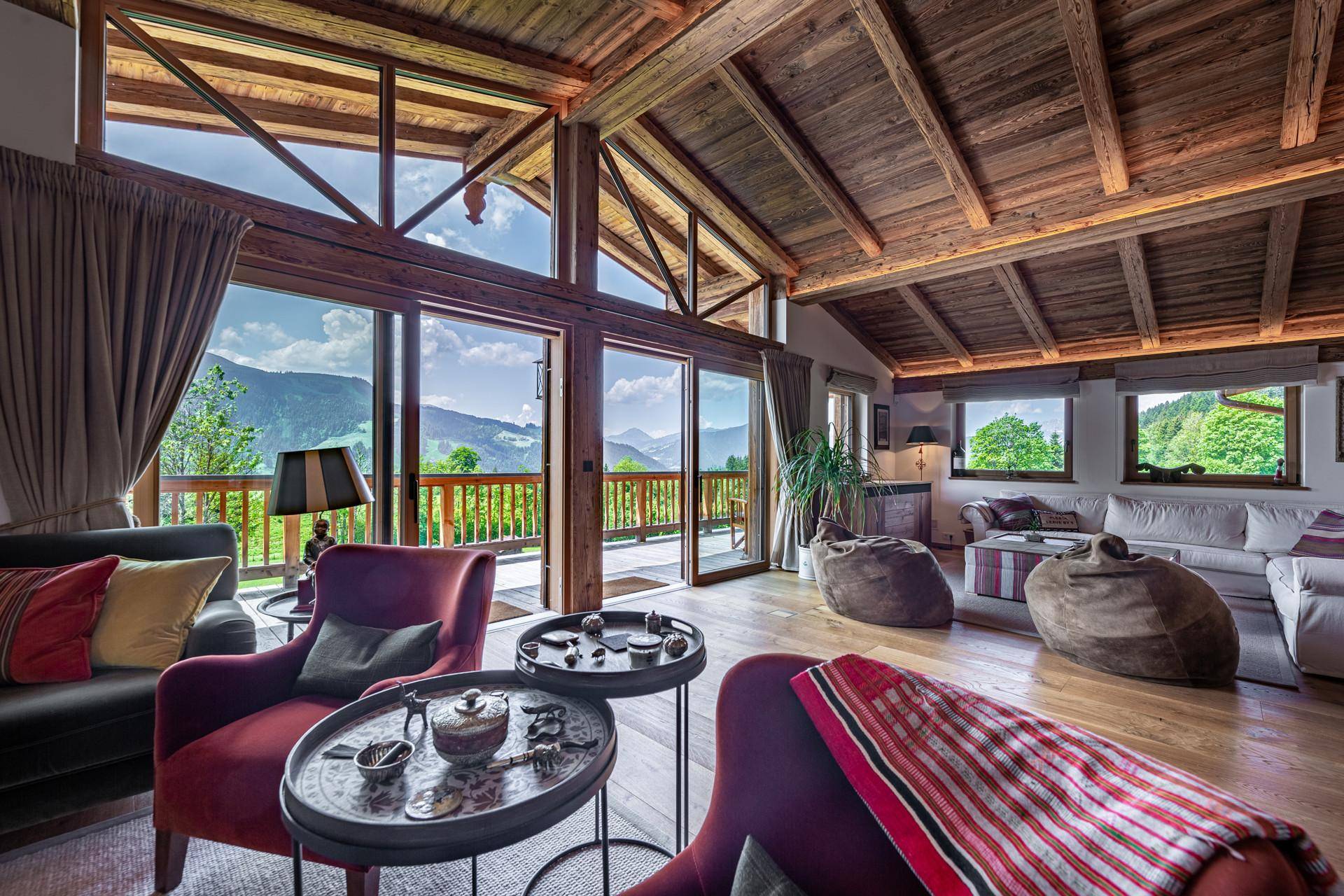 Gemütliches Wohnzimmer im alpinen Stil mit hohen Holzdecken, großen Fenstern und atemberaubendem Bergblick.
