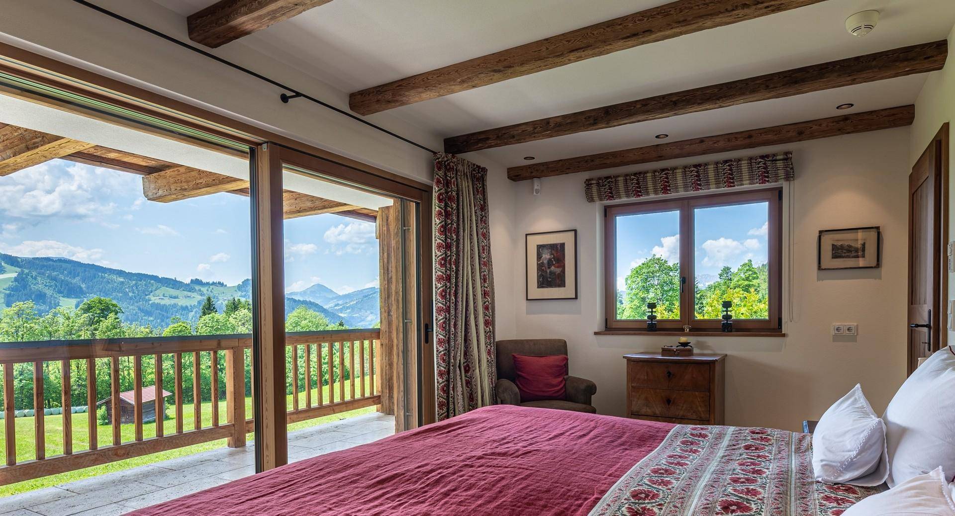 Schlafzimmer mit Holzbalken, großem Bett und direktem Zugang zu einem Balkon mit malerischem Bergblick.
