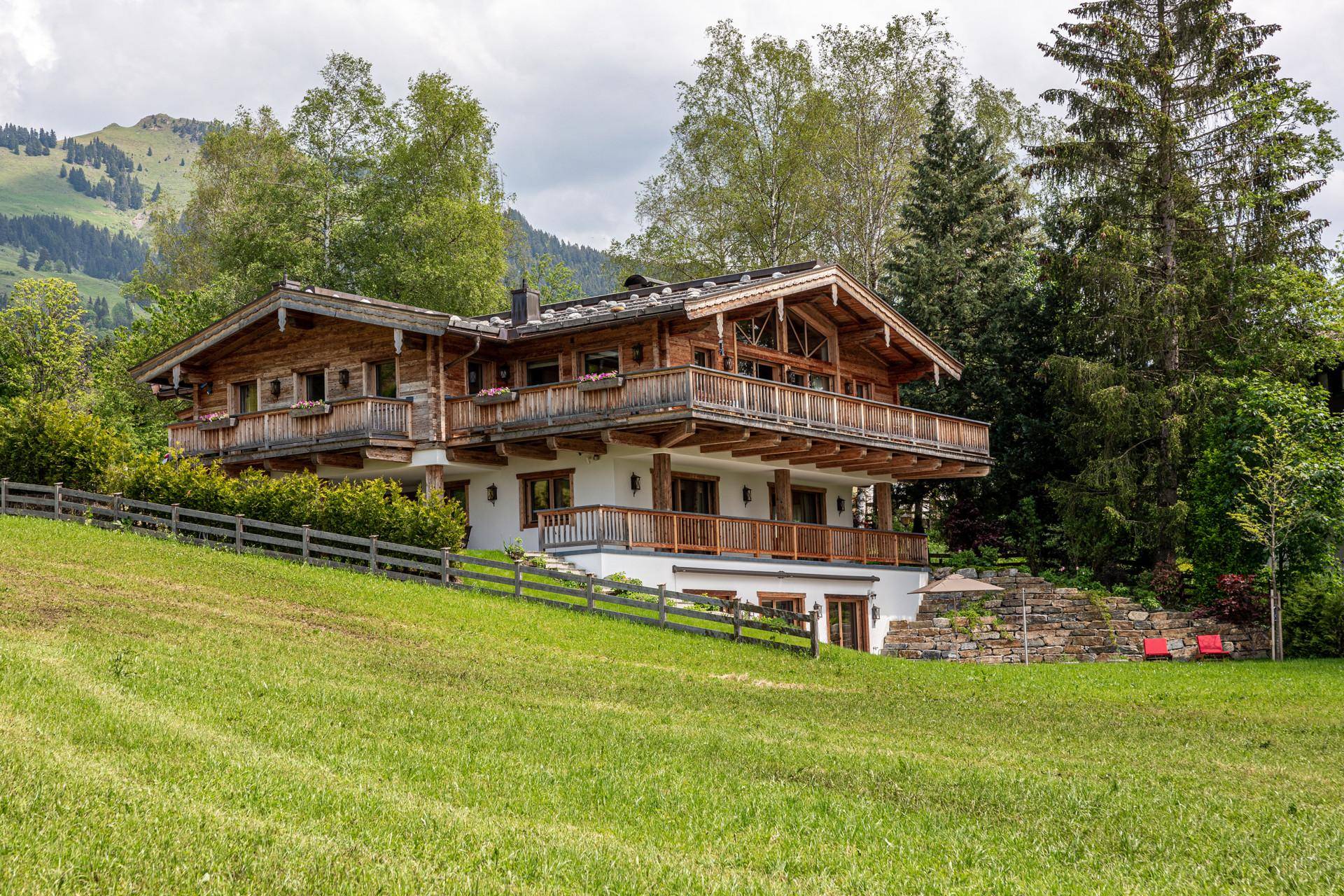 Charmantes Chalet-Haus auf einem grünen Hügel, umgeben von Bäumen, mit traditioneller Holzfassade und Balkonen.