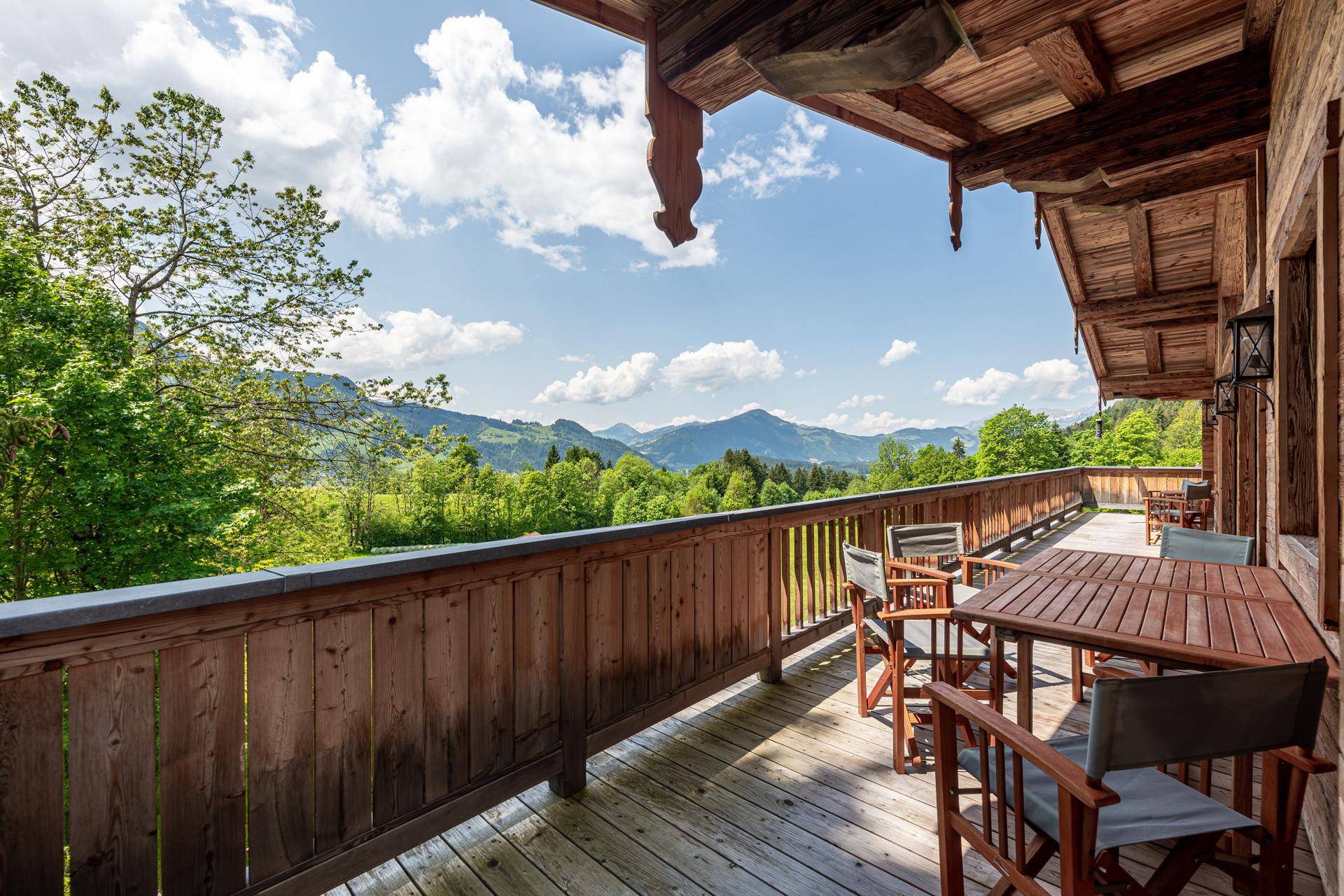 Langer Holzbalkon mit Esstisch und Stühlen, der einen weiten Panoramablick auf die Berge bietet.