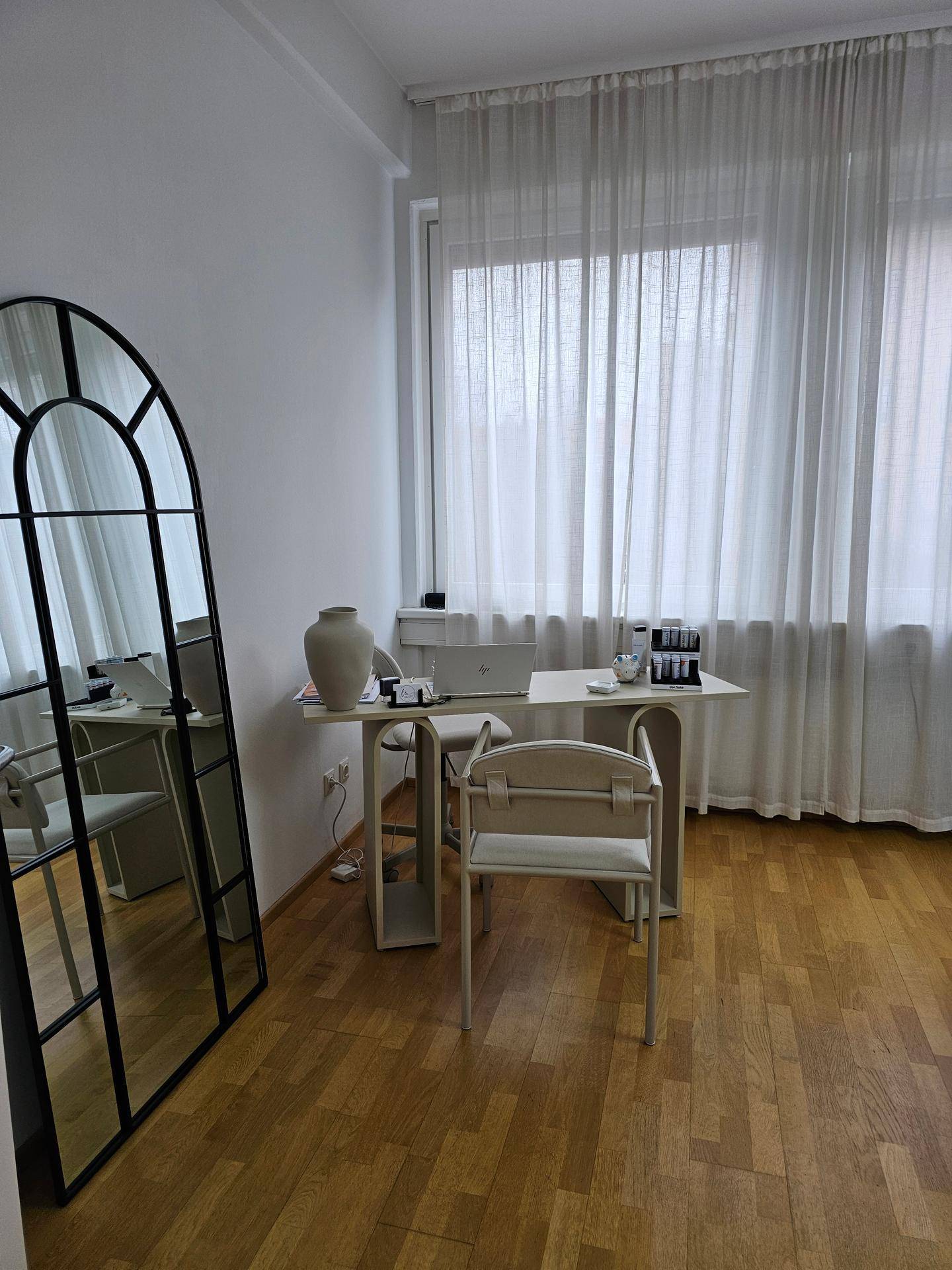 Heller Empfangsbereich mit großem Spiegel, modernem Schreibtisch und Vorhängen vor dem Fenster.