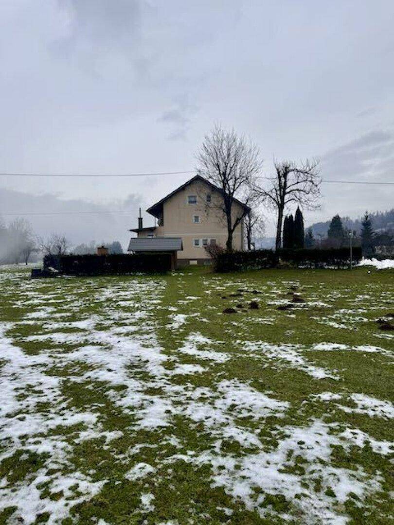 Wohnhaus mit Satteldach, umgeben von einer teilweise schneebedeckten Wiese an einem bewölkten Tag.
