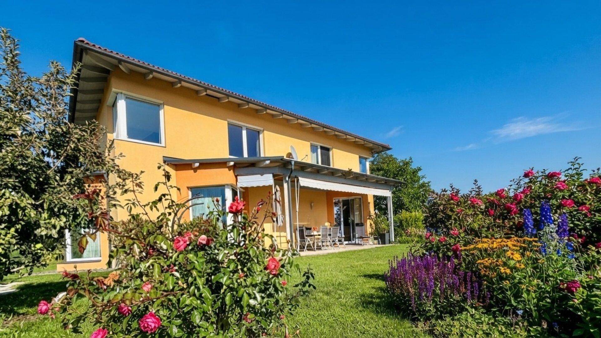 Gelbes Haus mit blühendem Rosengarten und grüner Rasenfläche unter blauem Himmel.