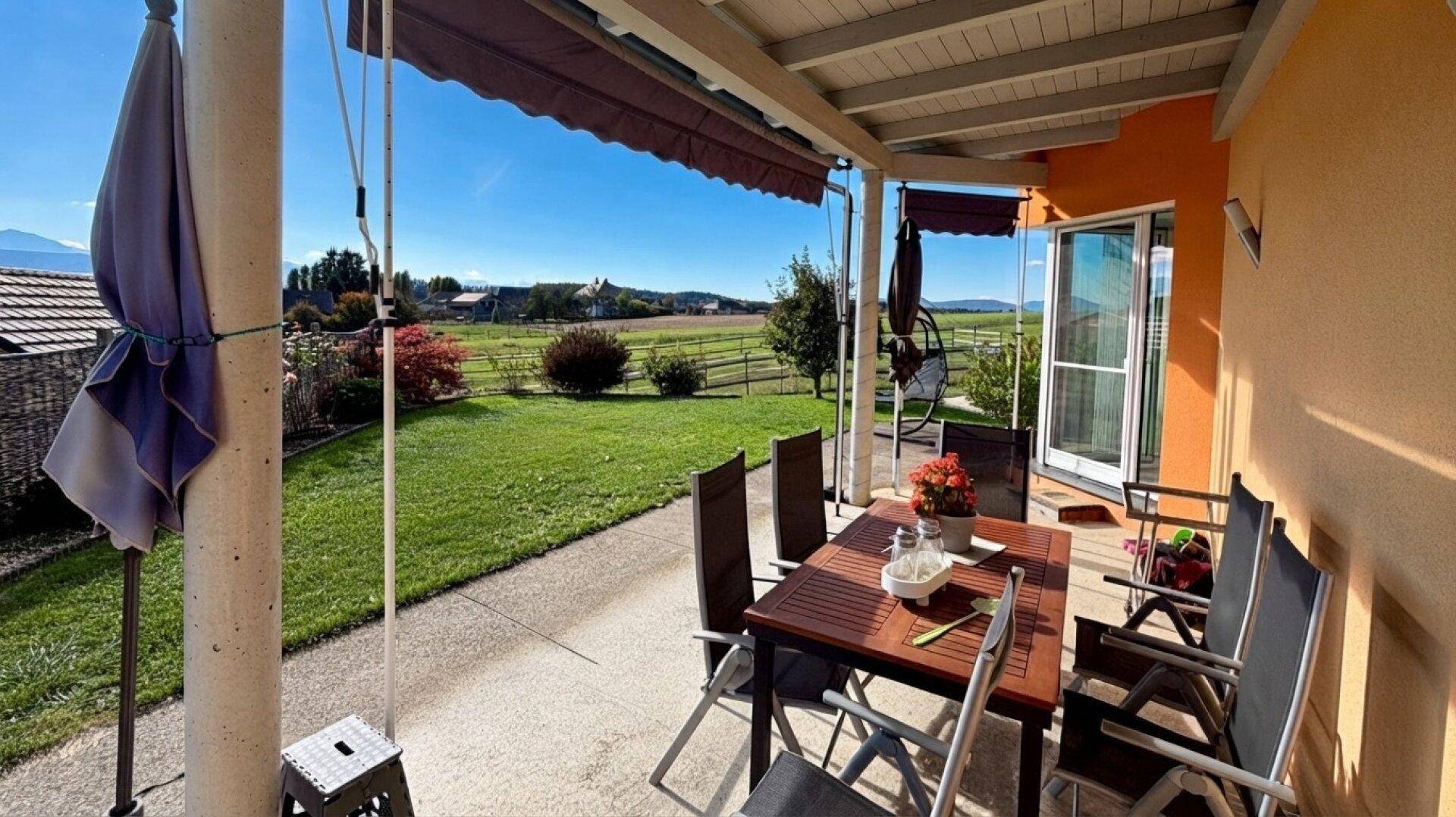 Überdachte Terrasse mit Esstisch und Stühlen, bietet weiten Blick ins Grüne.