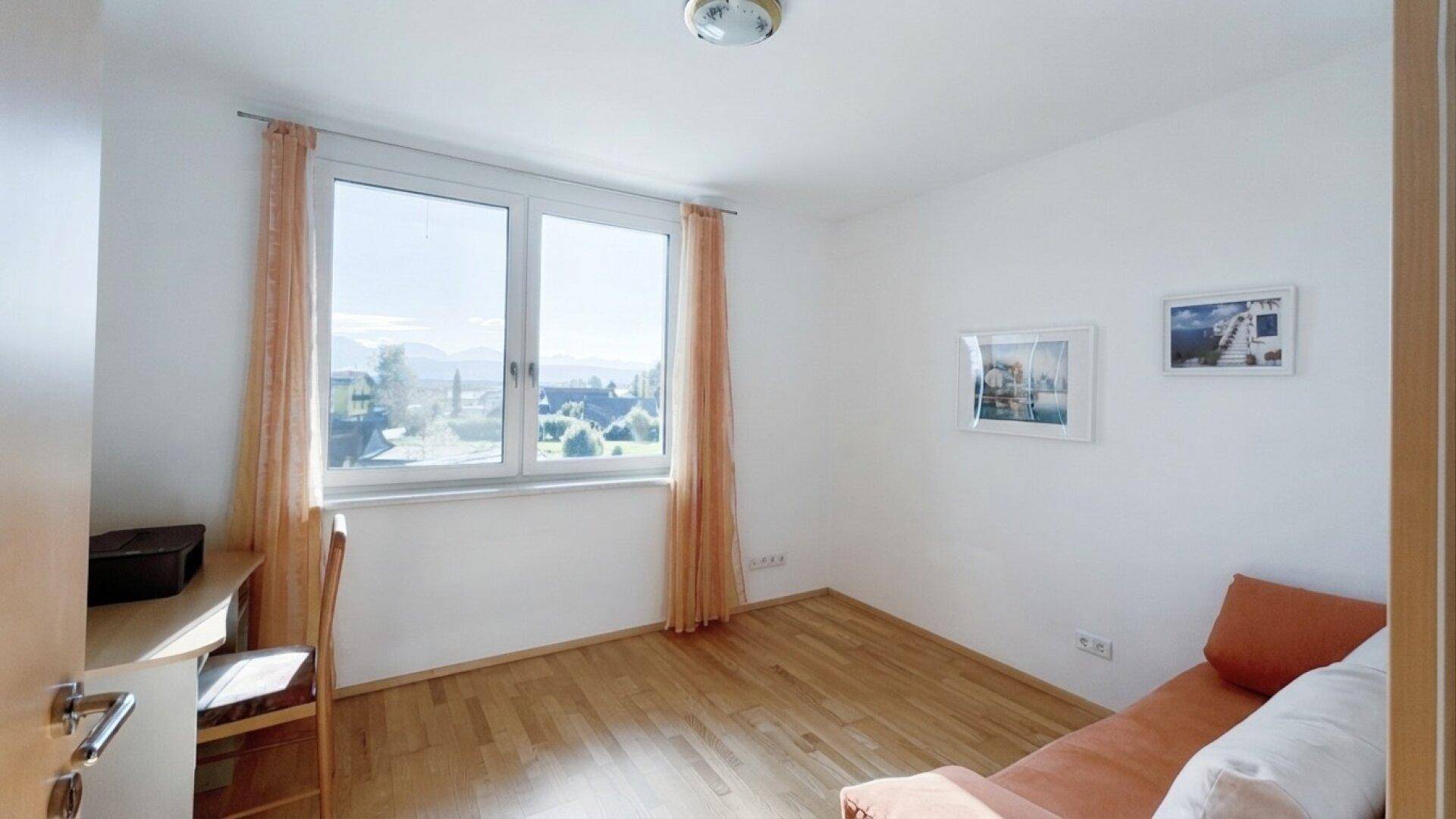 Helles Schlafzimmer mit Holzboden, Schreibtisch und Fenster mit Bergblick.