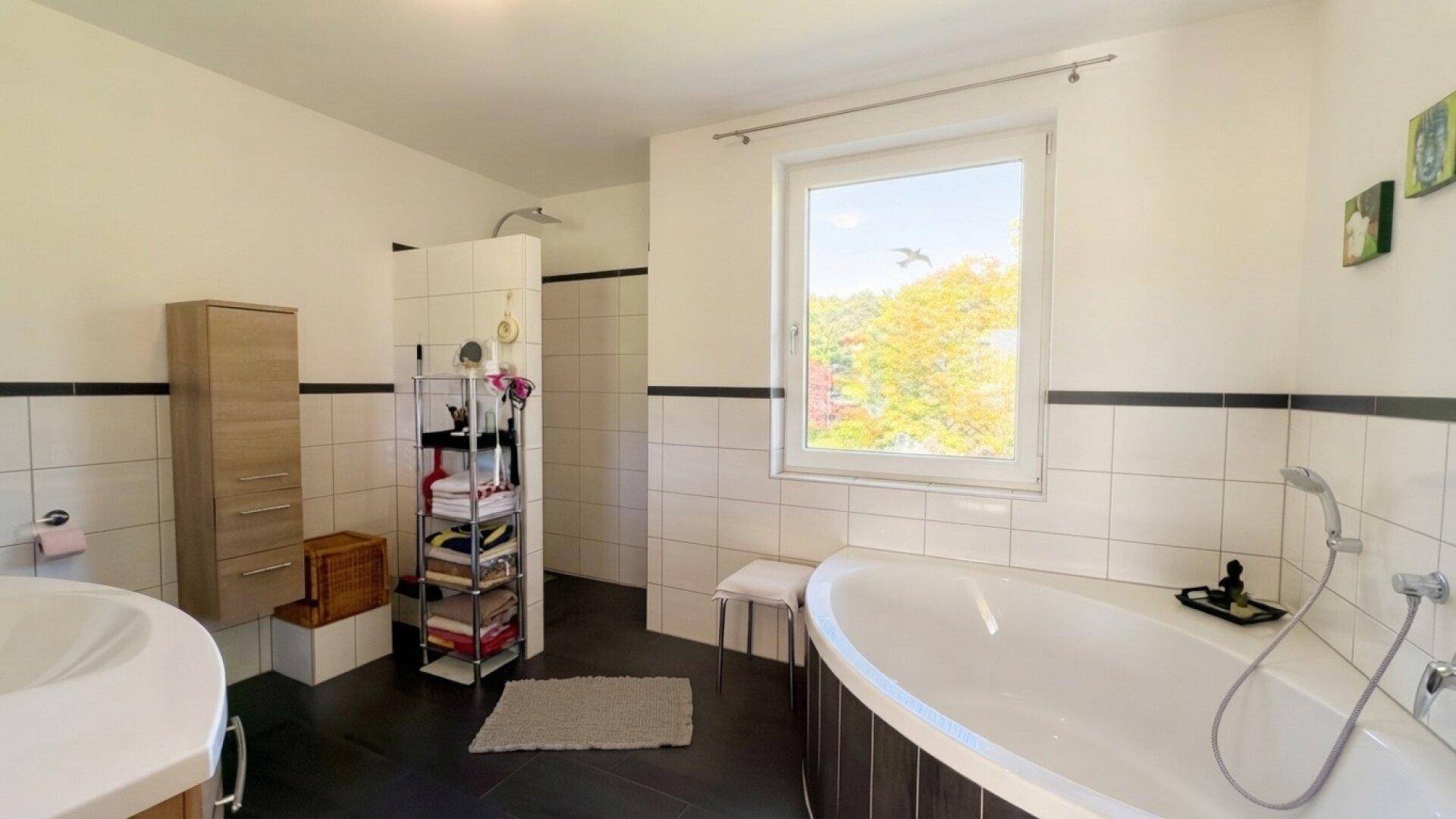 Geräumiges Badezimmer mit Badewanne, Dusche und Fenster für Tageslicht.