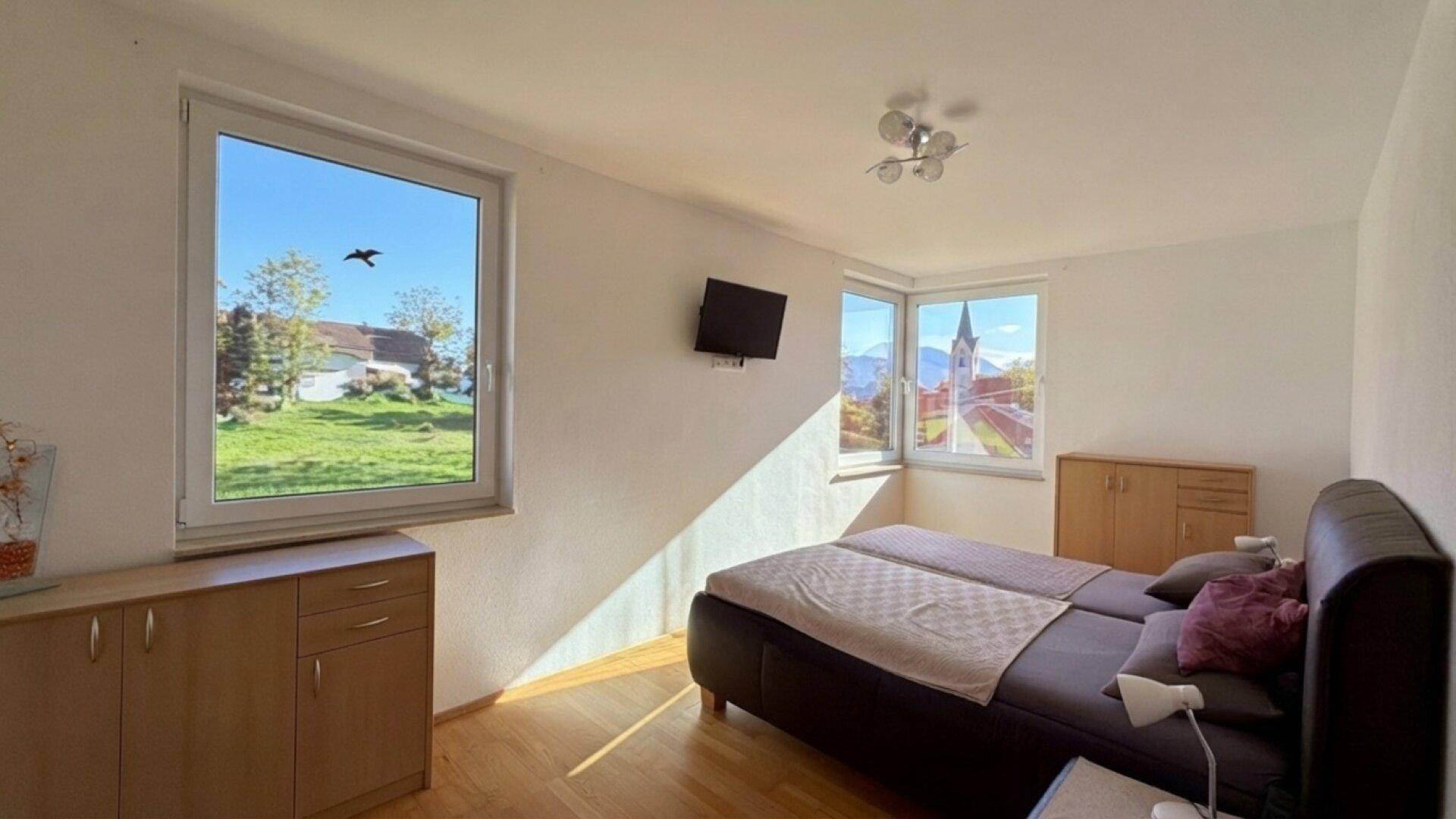 Schlafzimmer mit Holzboden, Doppelbett und Fenstern mit Blick auf die Umgebung.