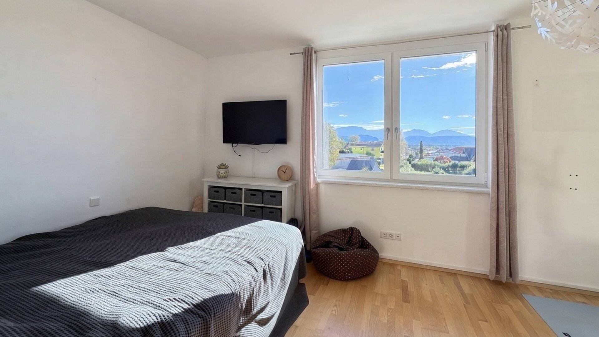 Schlafzimmer mit Holzboden, Bett und großem Fenster mit weitem Ausblick.