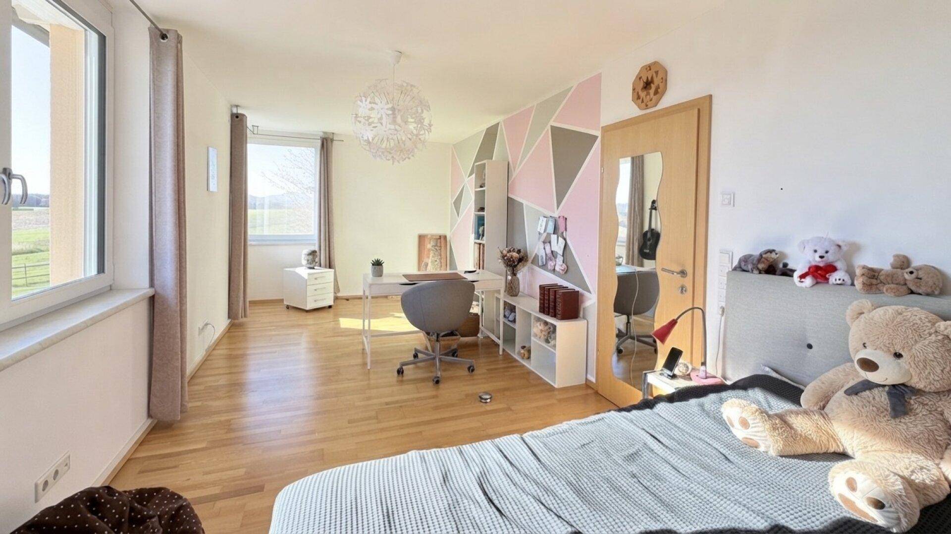 Helles Zimmer mit Holzboden, Schreibtisch und farbiger Wandgestaltung.