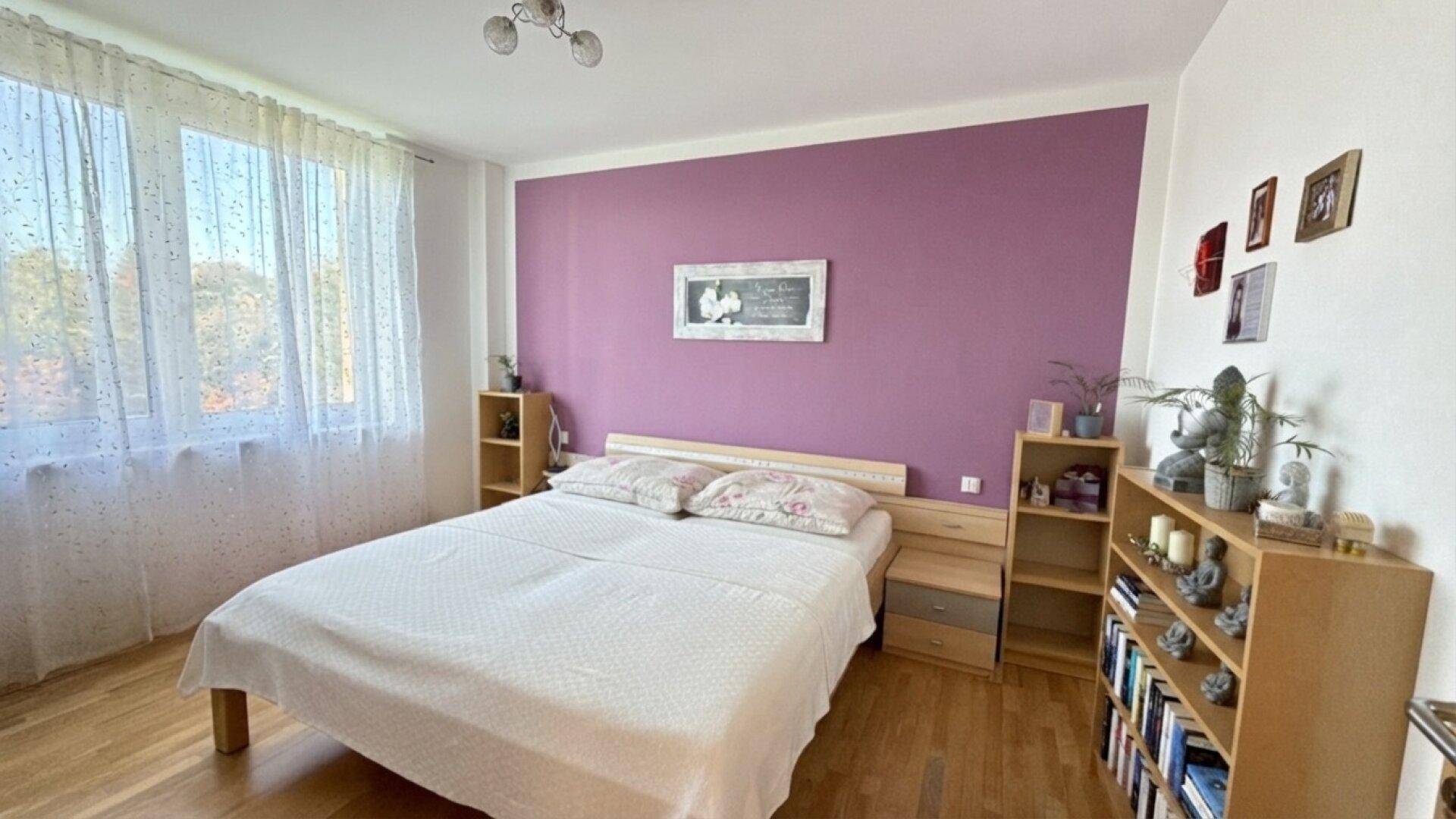 Schlafzimmer mit Holzboden, Doppelbett und violetter Akzentwand.