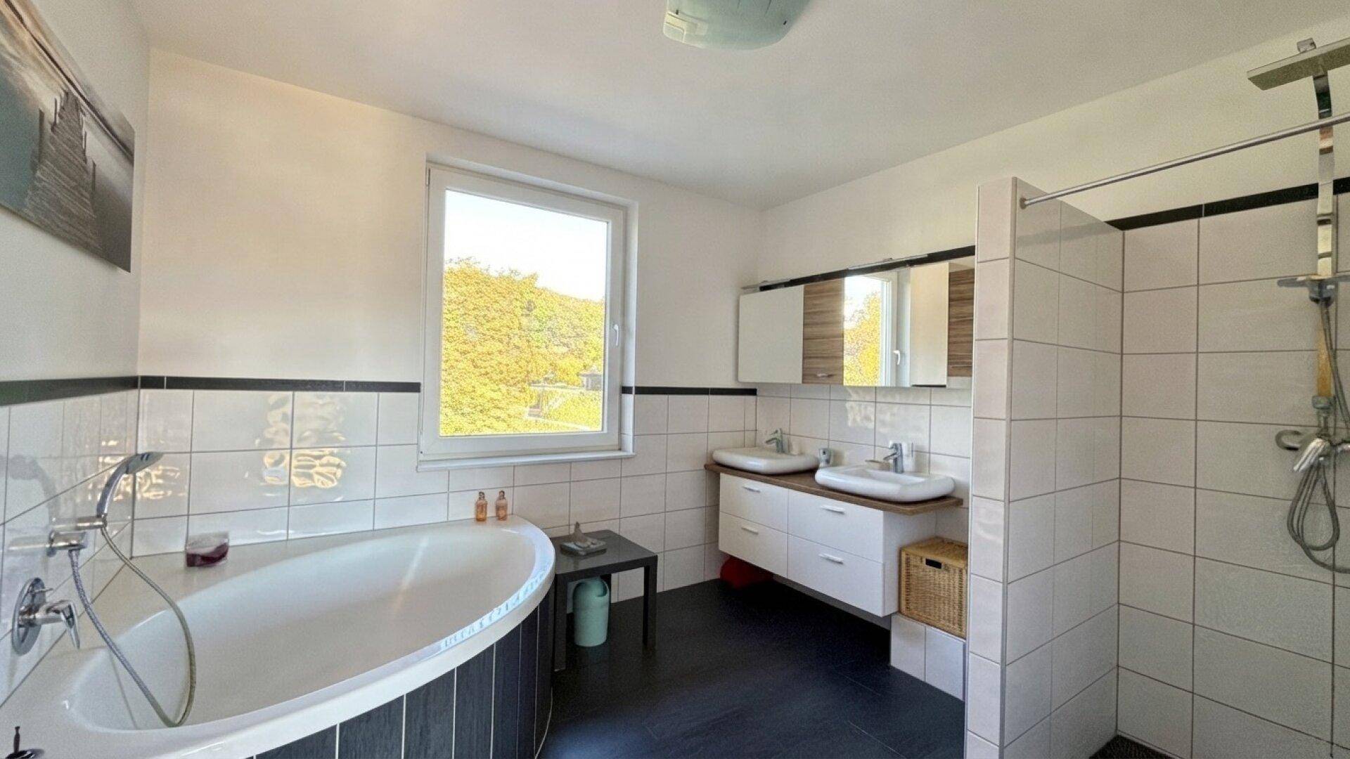 Modernes Badezimmer mit Badewanne, Dusche, Doppelwaschbecken und Fenster.